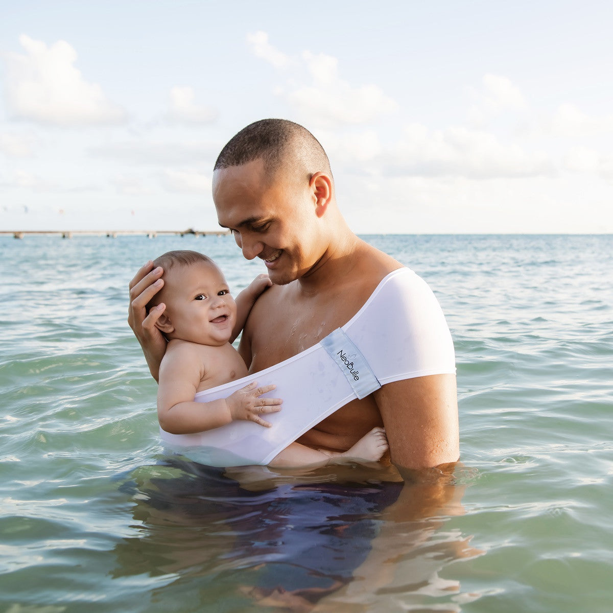 Pai a segurar um bebé no mar, ambos a utilizar o Aquabulle branco.