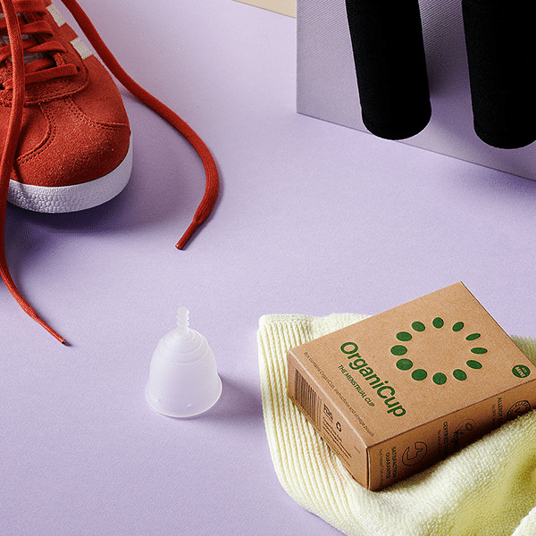 Copo menstrual OrganiCup Mini junto a sapatilha desportiva.