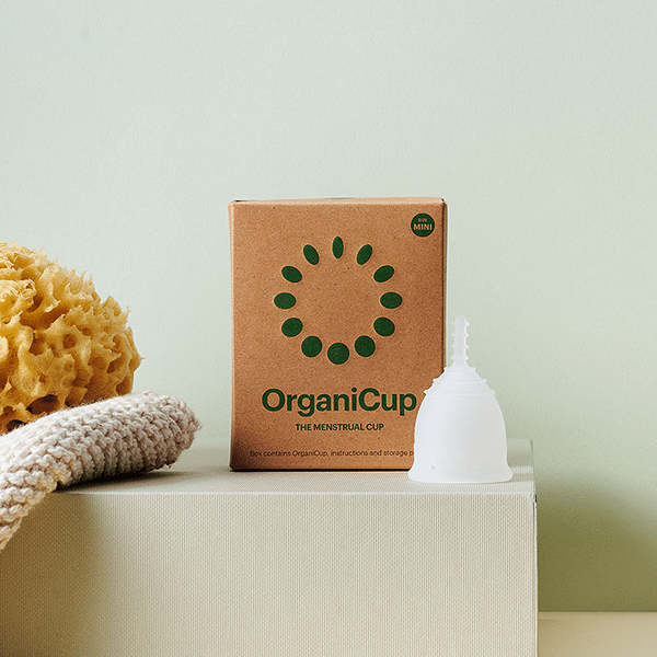 OrganiCup Mini com esponja natural sobre caixa de cartão.