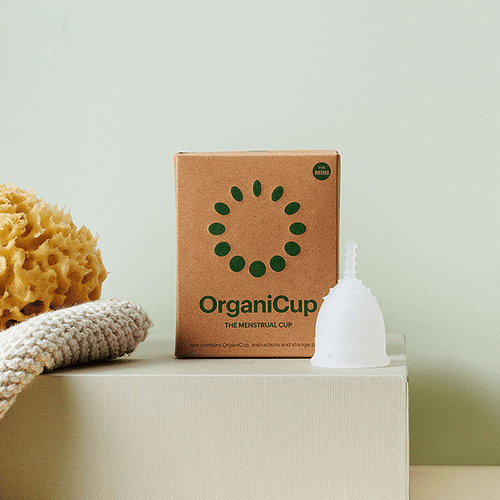 OrganiCup Mini com esponja natural sobre caixa de cartão.