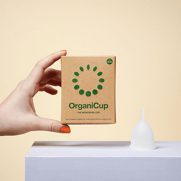 Mão feminina segurando a caixa do OrganiCup Mini com o copo ao lado.