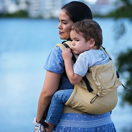 Mulher de lado, carregando um bebé na Mochila Neko Switch, destacando o conforto e o suporte ergonómico.