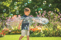 Criança brincando com um grande círculo de bolhas de sabão geradas pelo Pustefix Multi Bubbler, num jardim ensolarado.