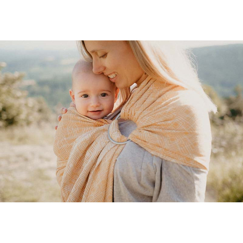 Mãe em ambiente externo usando o Sling de Argolas Neobulle, com bebé seguro e confortável.