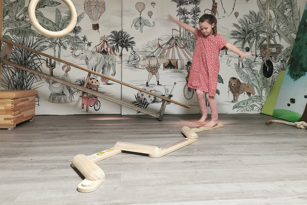 Criança a equilibrar-se num percurso de vigas de madeira "Adventure" da small foot, montado no chão da sala.