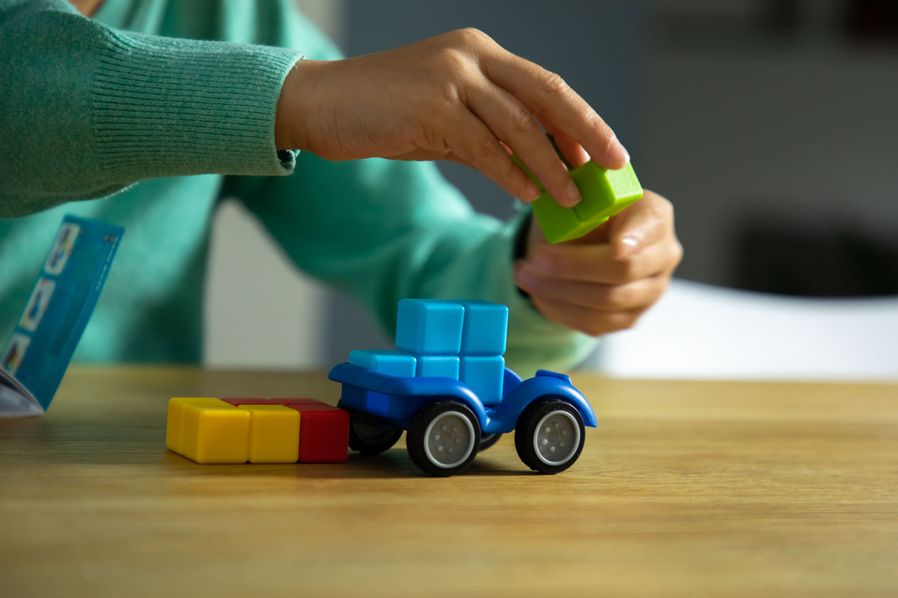 Mãos de uma criança a montar o SmartGames SmartCar Mini, mostrando o processo de construção e resolução de desafios.