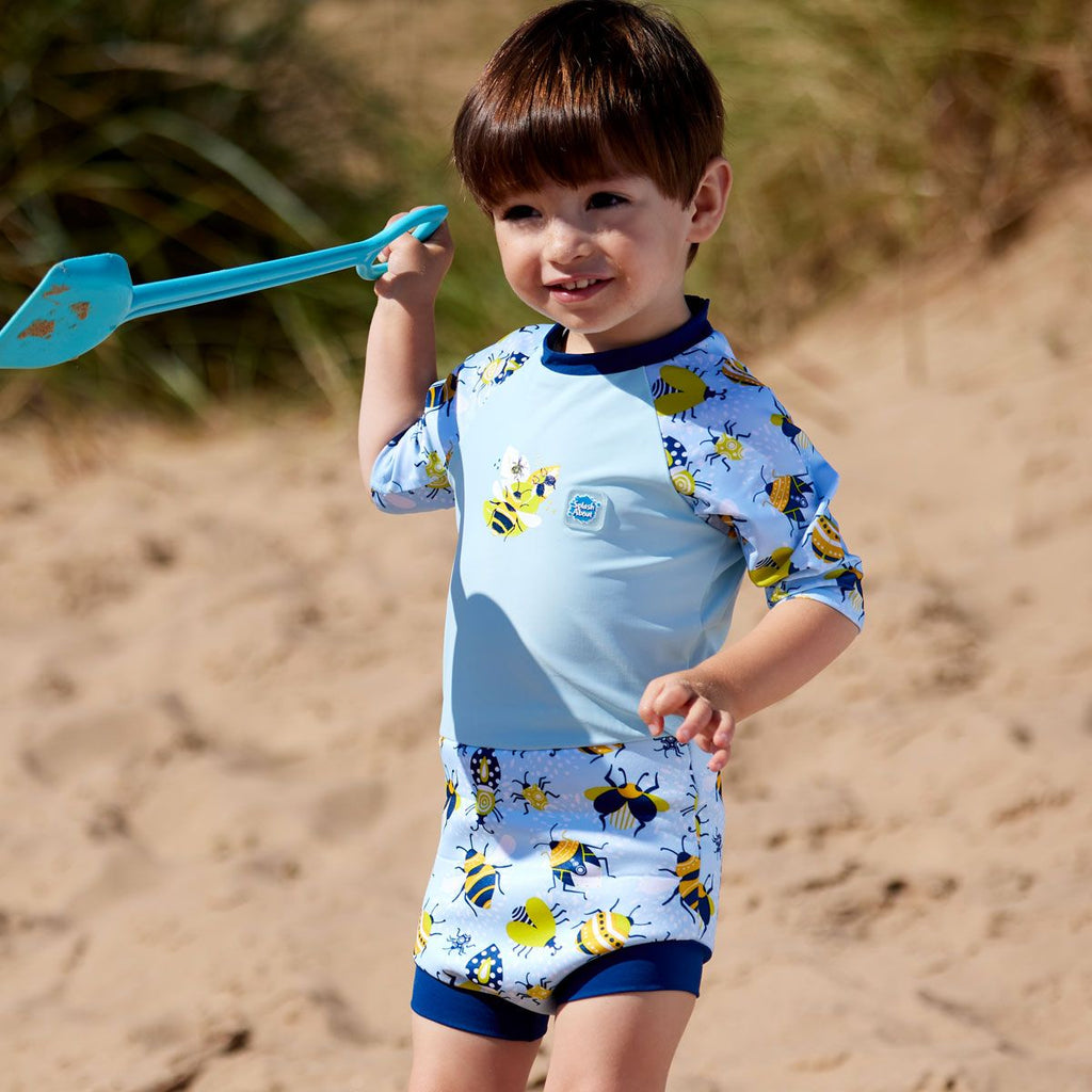 Fato de banho térmico Splash About Happy Nappy Sunsuit Bugs Life, com padrão de insetos, em destaque no corpo de um bebé a sorrir.
