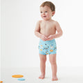Bebé sorridente a usar a fralda de natação reutilizável Splash About Happy Nappy Noah's Ark, em azul claro com padrão.