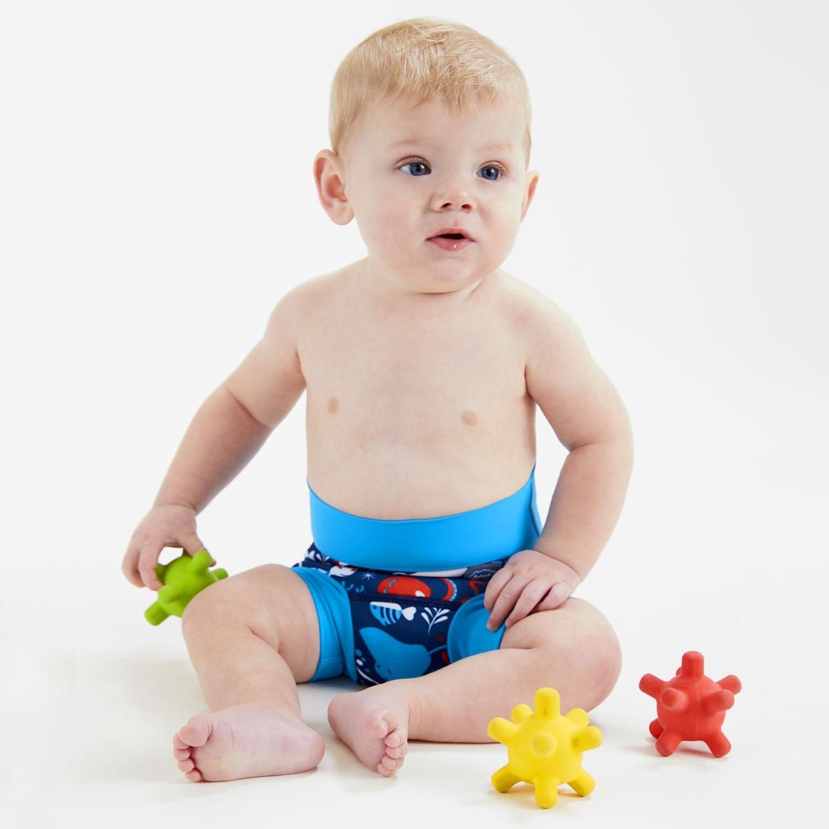 Bebé loiro sentado a brincar, a usar a fralda/cueca reutilizável Splash About Happy Nappy Under the Sea.