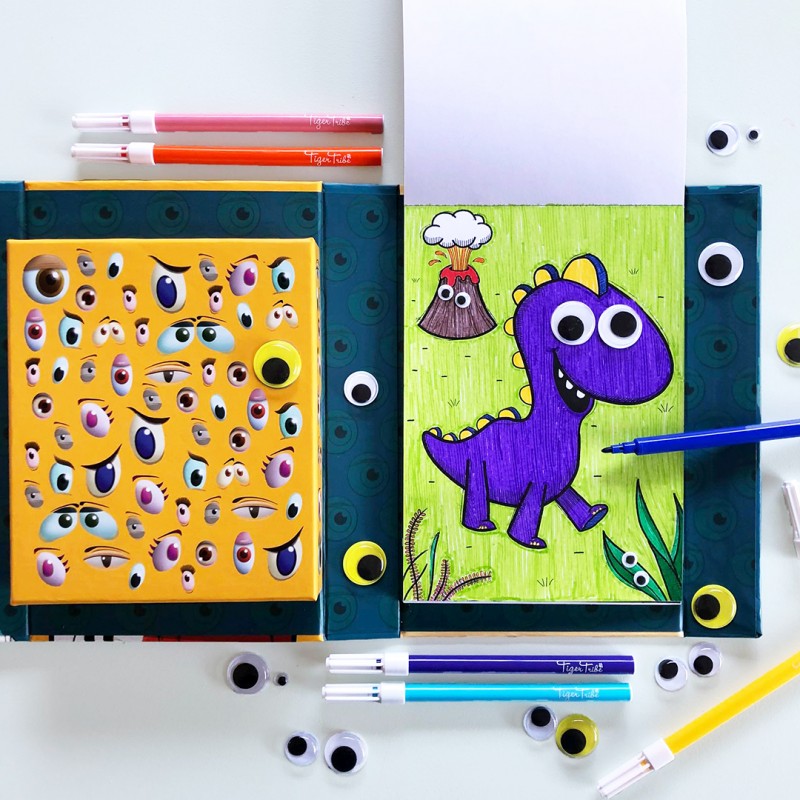 Criança a usar o conjunto Tiger Tribe "Crazy Eyes Creatures", a colorir e a adicionar olhos a um desenho de um dinossauro.