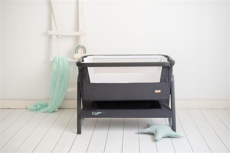Berço CoZee® Lite da Tutti Bambini em cinza, montado junto a uma cama de casal, com lateral rebatida para co-sleeping.