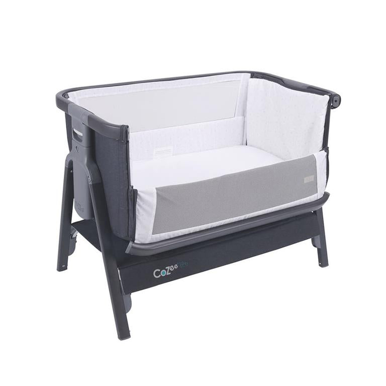 Berço CoZee Lite da Tutti Bambini em cinza, montado, mostrando o design next-to-me com lateral rebatida junto a uma cama de adulto.