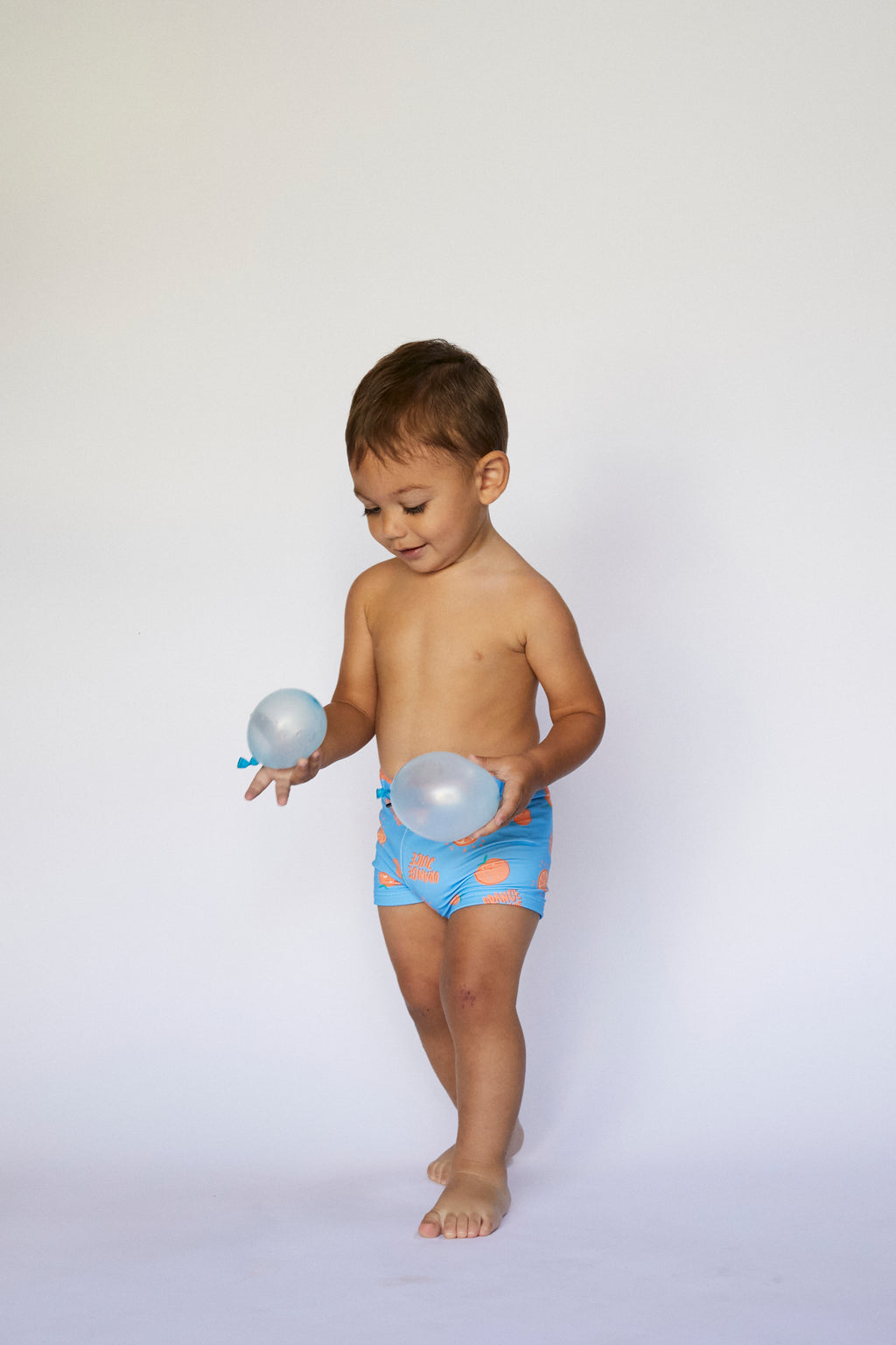 Menino em pose de brincadeira, vestindo o calção de lycra Waterlemon azul com laranjas, ideal para piscina.