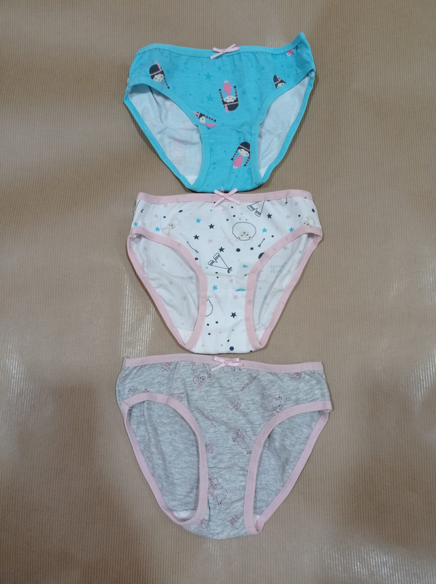 Três cuecas para criança, em tons azul, branco e cinzento, sobrepostas numa superfície castanha. As cuecas mostram detalhes das estampas.