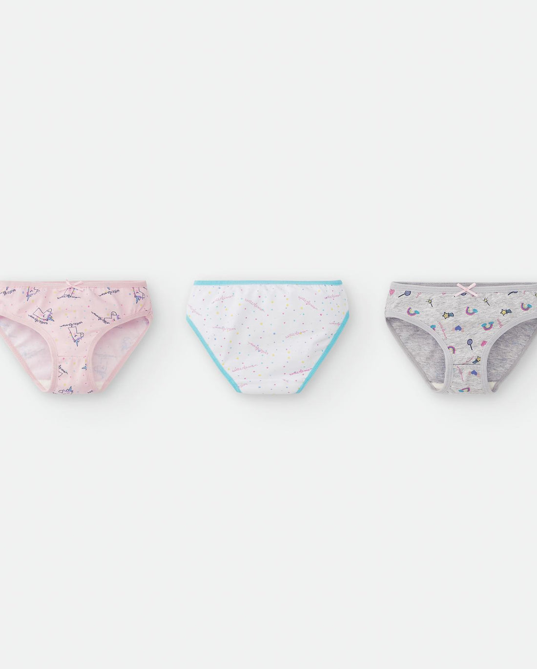 Três cuecas para criança, em tons rosa, azul e cinzento, dispostas em linha sobre fundo branco. Cada cueca tem uma estampa diferente: unicórnios, estrelas e varinhas de condão.