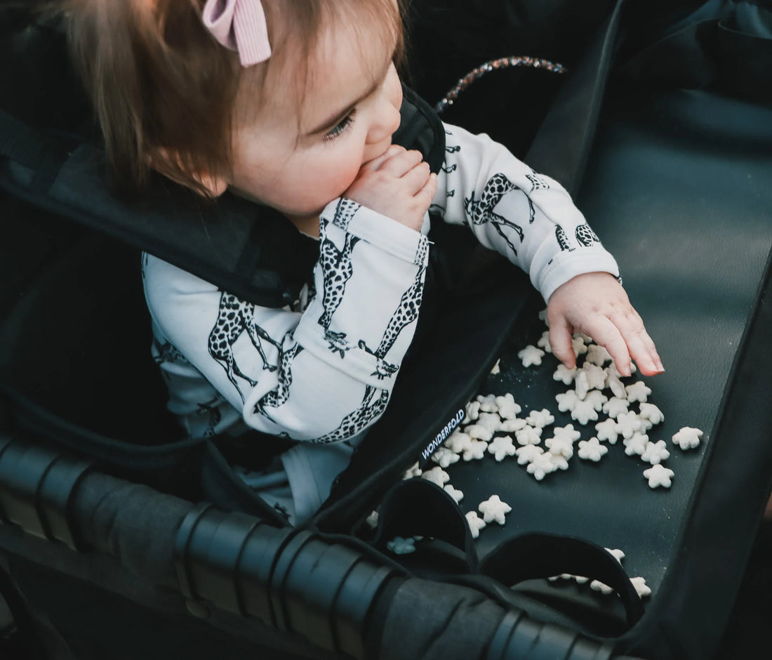 Criança feliz a comer snacks de um tabuleiro no interior de um carrinho vagão Wonderfold.